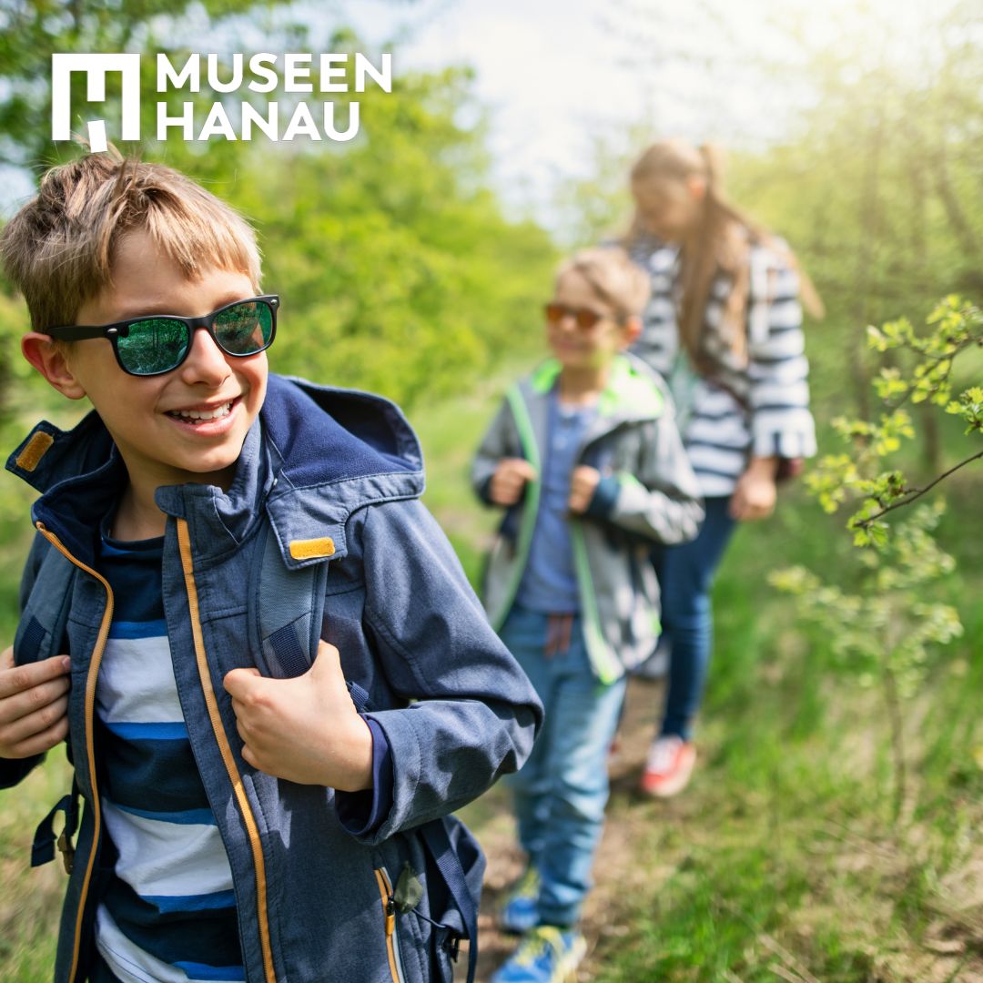 Familie wandert im Wald. Die beiden Jungen tragen Sonnenbrillen und lachen.